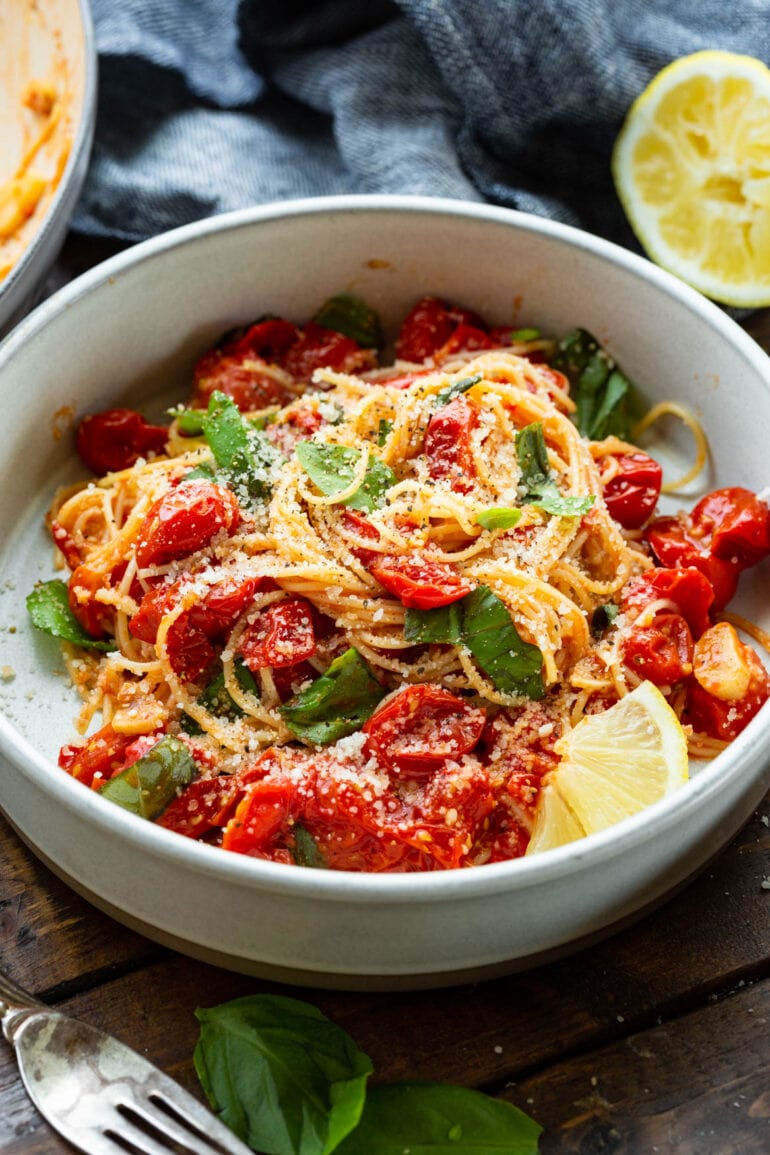 a photo of a bowl of cooked angel hair pasta toss with sauteed cherry tomatoes, fresh basil and a slice of fresh lemon.