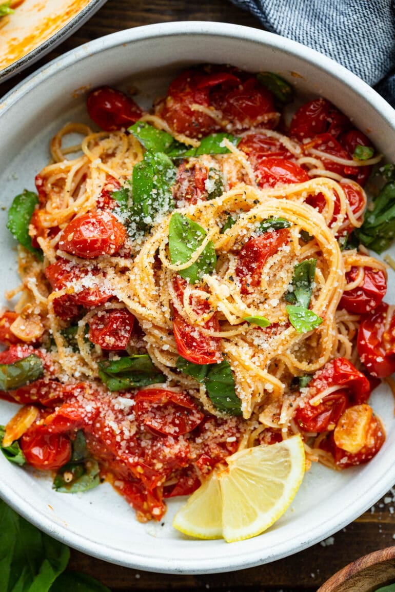 a photo of an italian dish with fresh basil, sauteed cherry tomatoes and a slice of lemon on the side