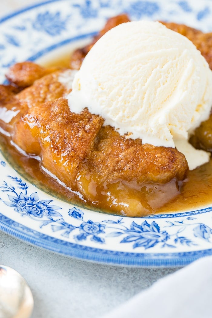 a blue china plate with two apple dumplings and caramel sauce with vanilla ice cream on top