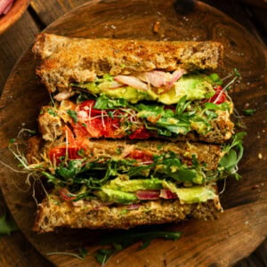 a photo of an avocado sandwich that has been cut in half and then set up on their side so you can see the layers inside the sandwich