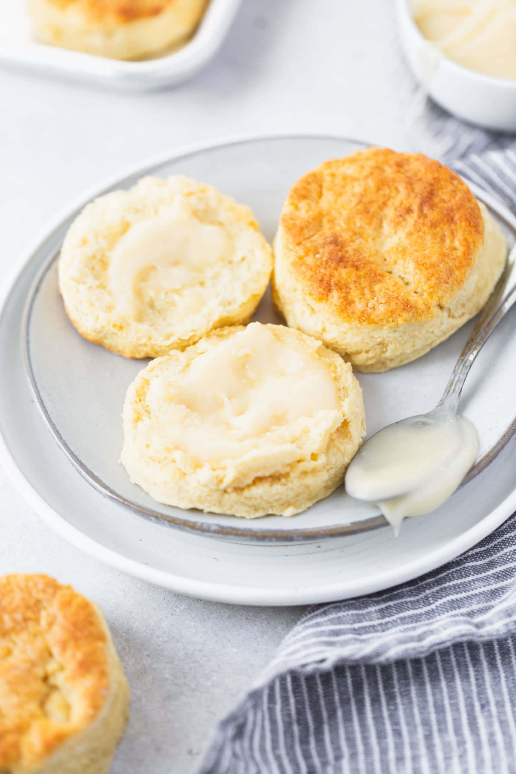 Buttermilk Biscuits Two buttermilk biscuits on a small white plate. One biscuit is broken in half and has been buttered.