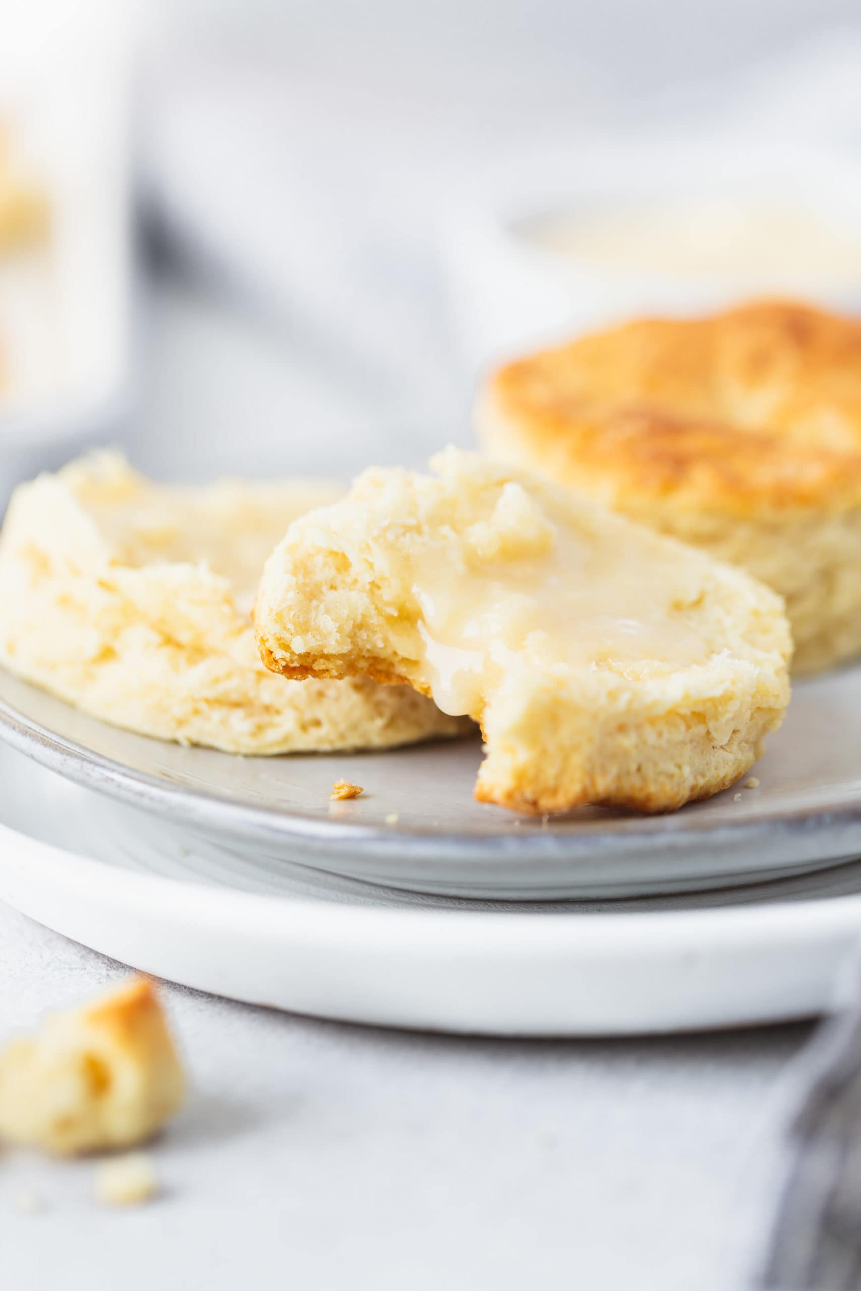 Buttermilk Biscuits Two buttermilk biscuits on a plate. One biscuit is broken in half and has been spread with honey butter. A bite has been taken from one of the halves.