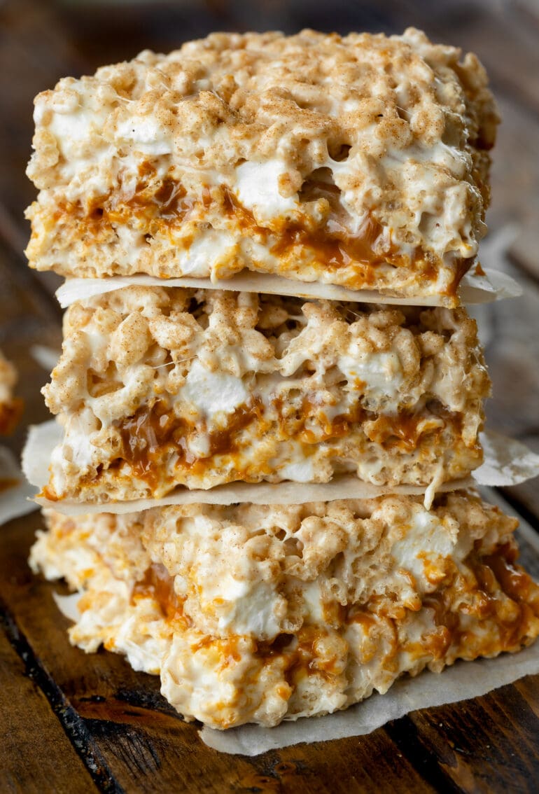 a photo of three dulce de leche stuffed gooey rice krispie treats stacked on top of each other with little pieces of parchment paper between them.