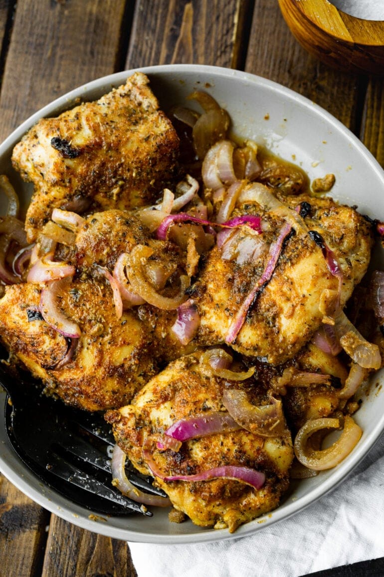 several golden baked chicken thighs mixed with slices of red onion.
