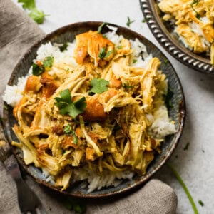 A metal, vintage bowl filled with white long grain rice and shredded chicken with a simple honey curry sauce made in an instant pot with cilantro on top. easy instant pot honey chicken