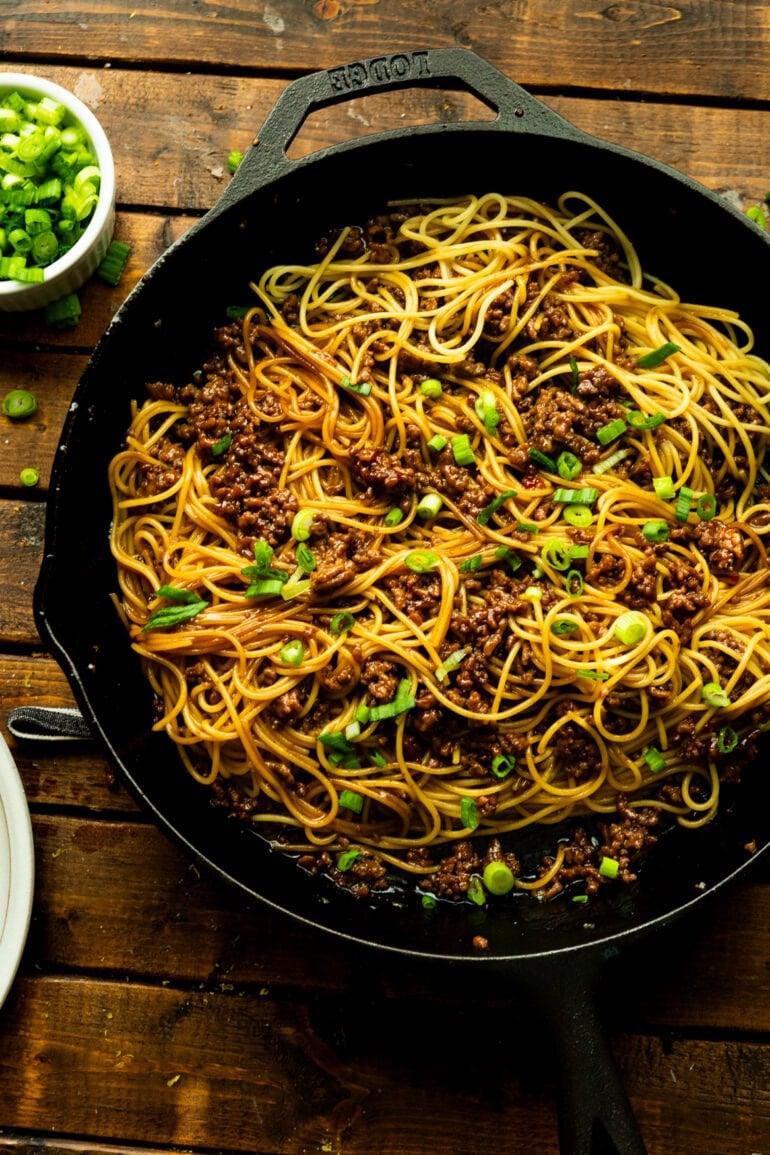 a photo of a cast iron skillet full of cooked spaghetti noodles tossed with ground beef and chopped scallions