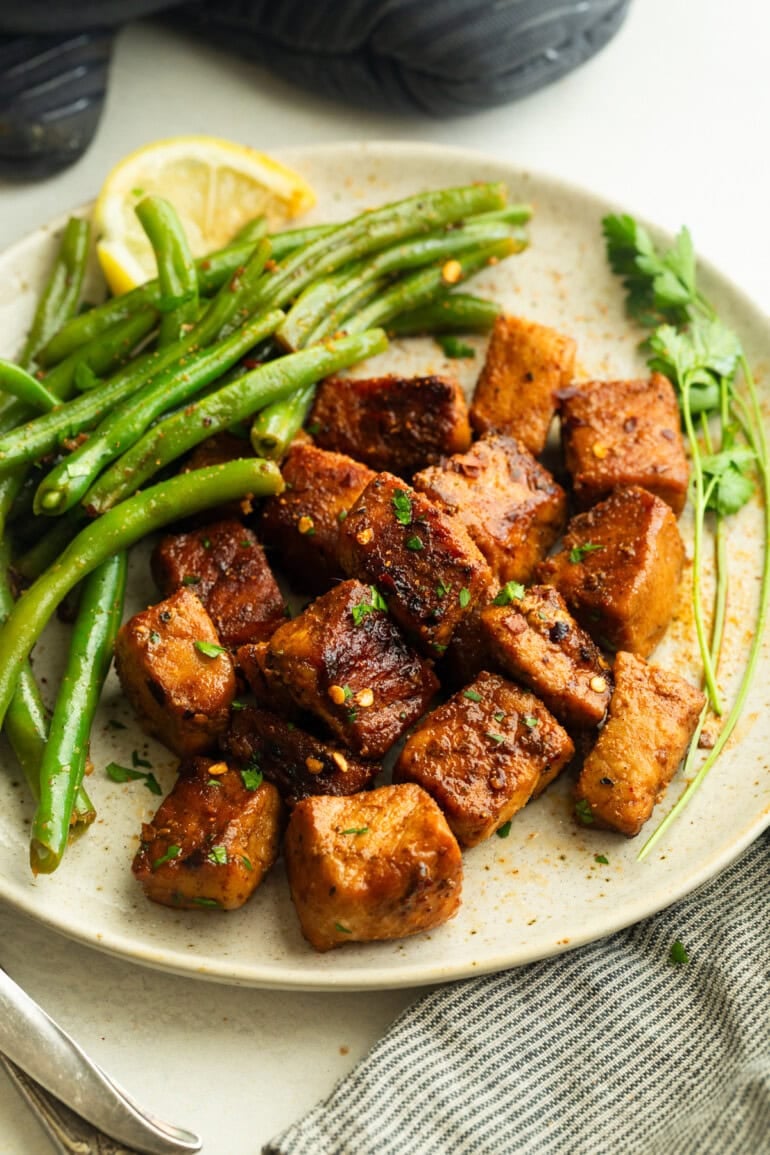 Overhead shot of juicy skillet pork bites and green beans, lightly sprinkled with herbs.