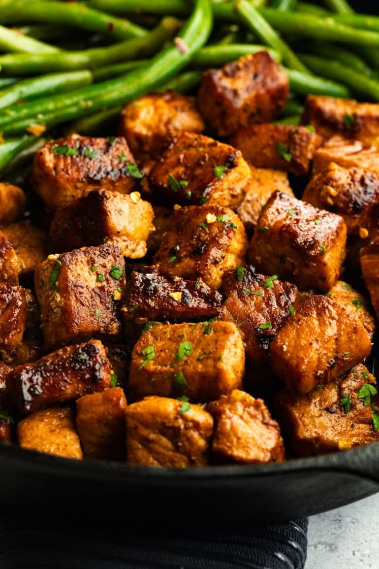 Close up of pan-fried pork and green beans plated together, showing texture and browning.