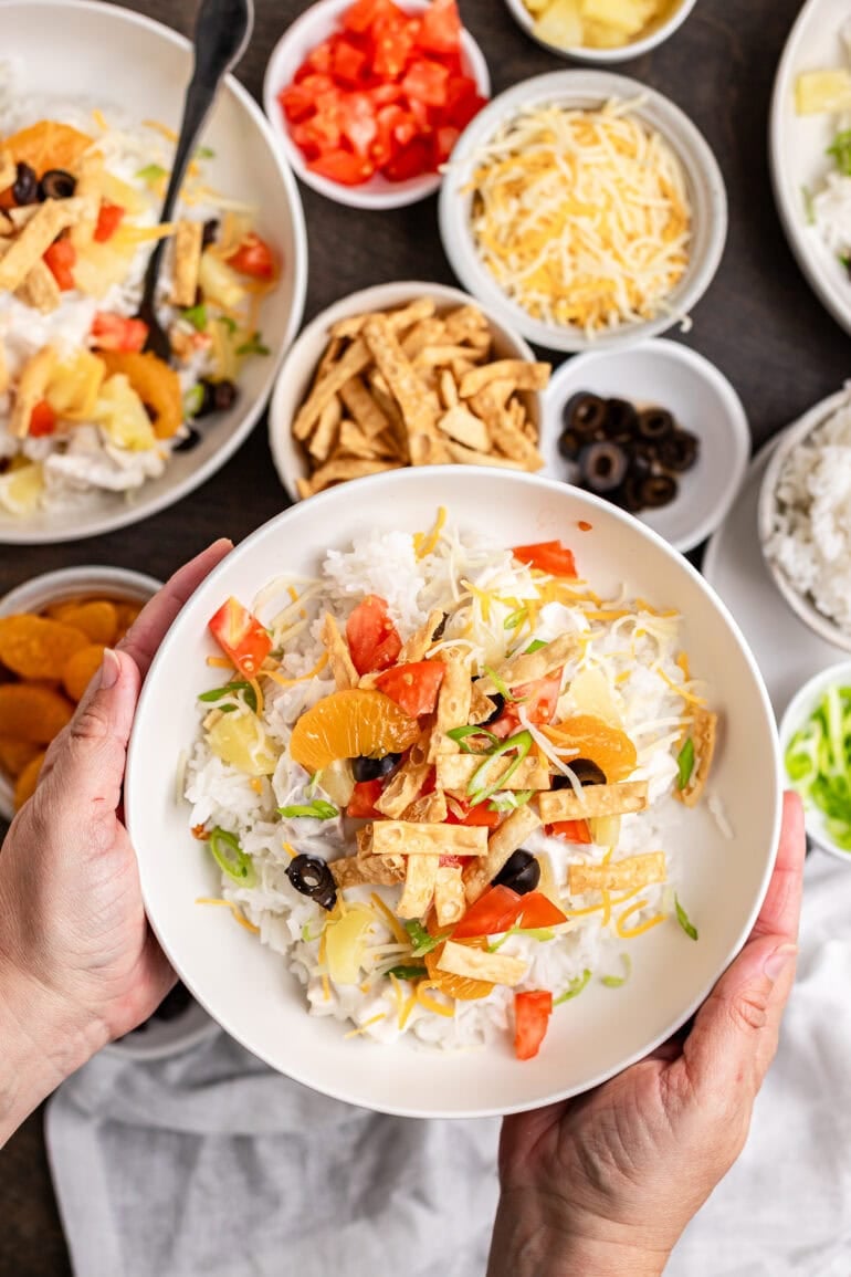 Ditch the soup cans and Chinese noodles, this is ultimate Hawaiian haystacks recipe and you're going to go crazy for them! A white bowl filled with Hawaiian Haystacks topped with pineapple chunks, cheddar cheese, green onions, and fresh tomatoes.