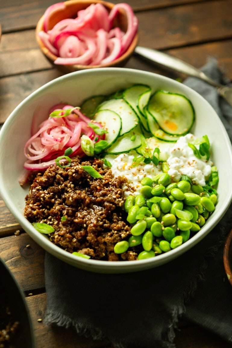 a photo of a bowl full of saucy korean ground beef with cottage cheese, edamame, pickled onions and thin slices of cucumbers