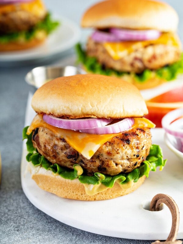 Three dinner plates containing chicken burgers on buns with lettuce cheese and red onions.