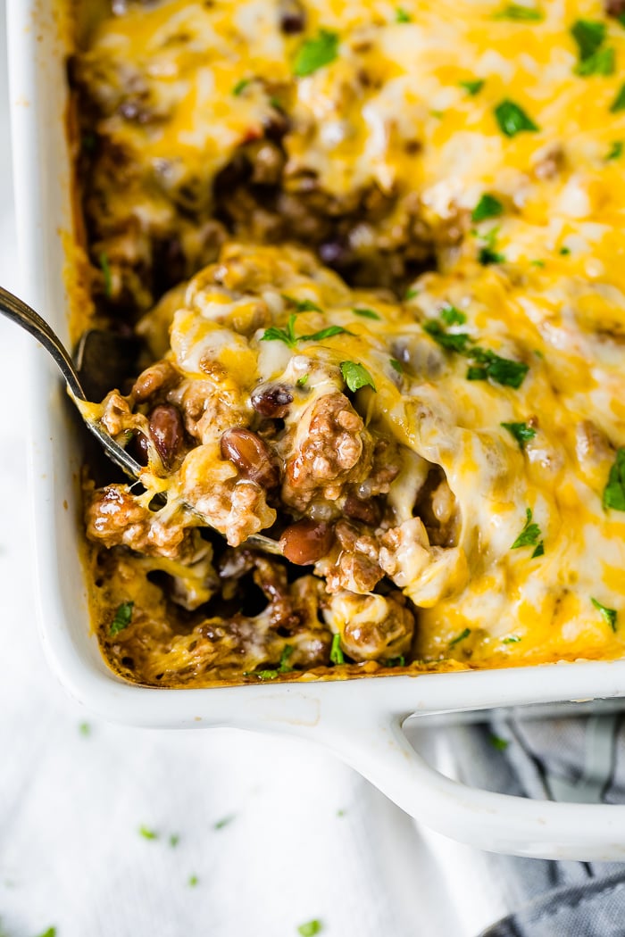 a white casserole dish with a Mexican ground beef casserole being scooped up with a large spoon
