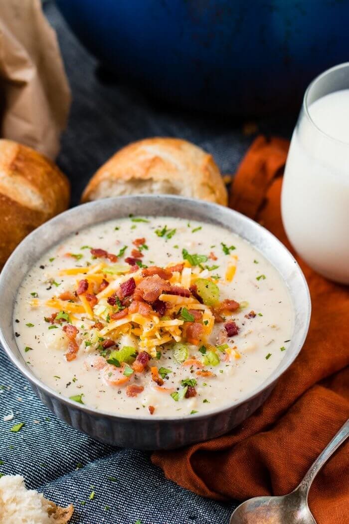 a bowl of creamy cauliflower soup with a glass of milk in the background and a couple of crusty rolls