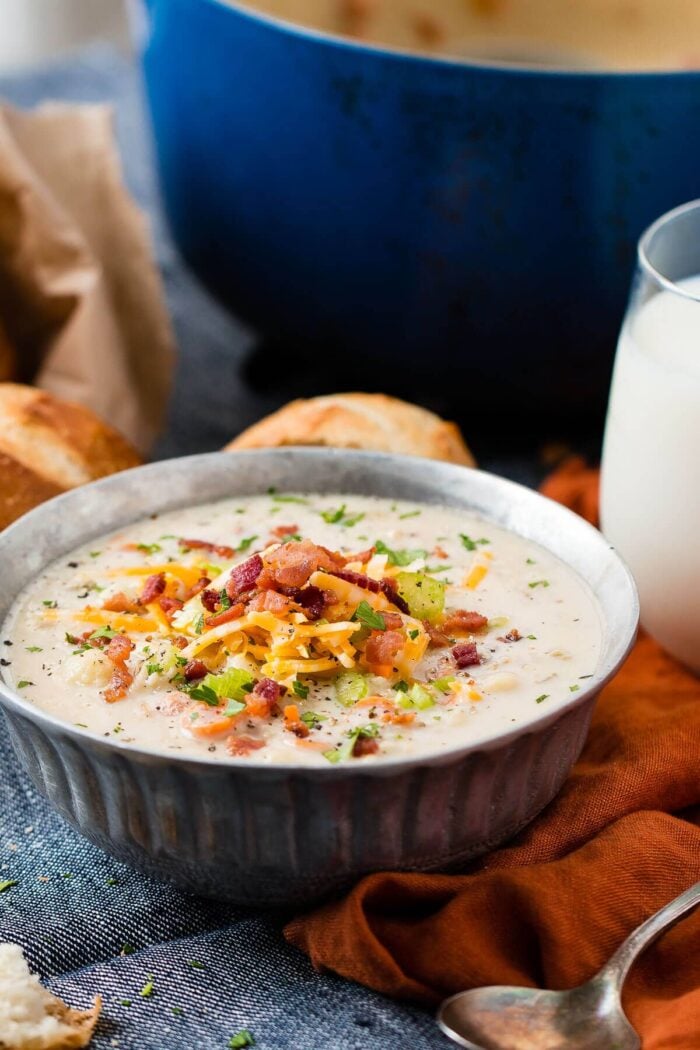 a large bowl of creamy cauliflower soup in a metal bowl topped with crispy bacon bits, sliced green onions and shredded cheddar cheese