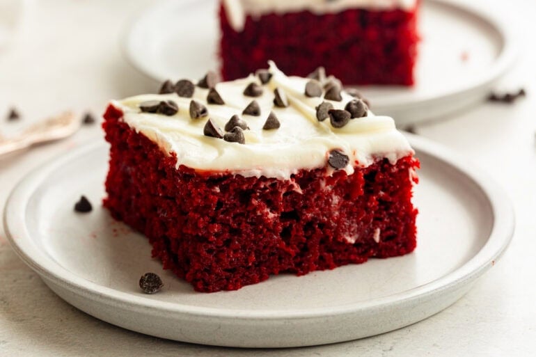 a piece of moist red velvet cake topped with white cream cheese frosting and sprinkled with mini chocolate chips