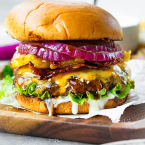 a photo of a cheeseburger topped with melted cheese, slice red onions, grilled pineapple, bacon and a white creamy sauce all in a toasted bun.