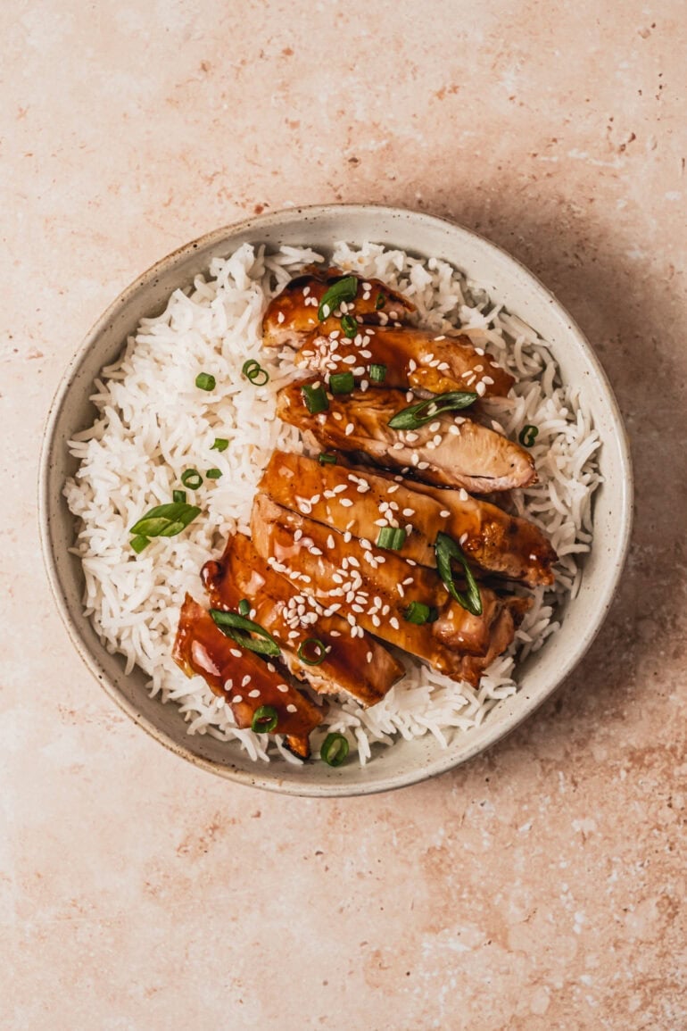 a plate of white rice topped with slices of teriyaki chicken