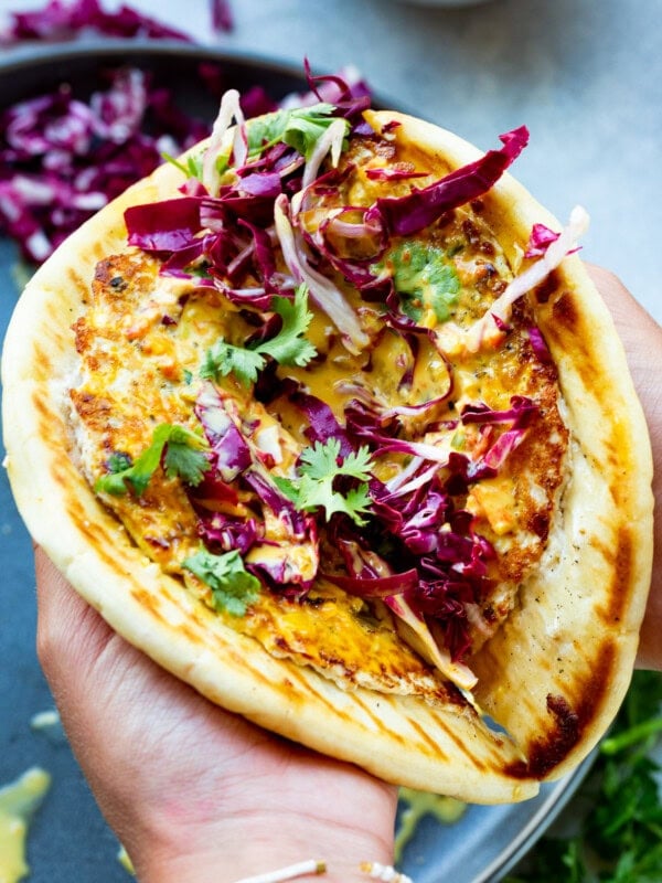 a piece of golden pita bread lined with a golden cooked ground chicken patty that is lathered in curry sauce and topped with radicchio and cilantro.