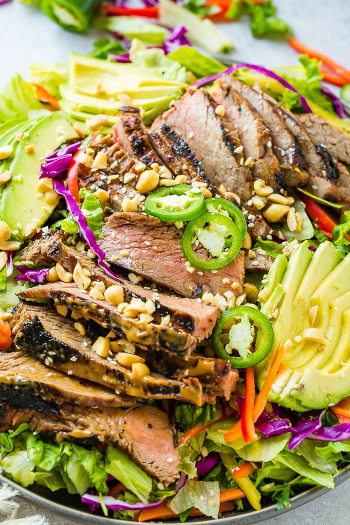A vibrate plate of Healthy Thai Peanut Salad with Grilled Flank Steak full of mixed greens, veggies and thai peanut sauce marinated steak with a ginger dressing and sesame seeds