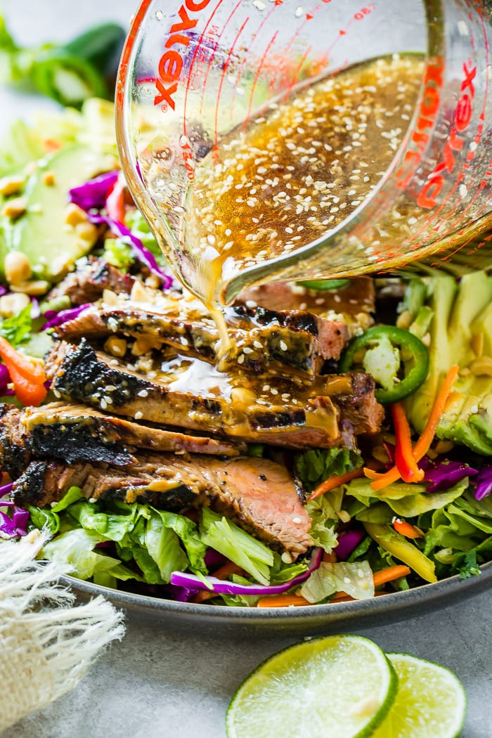 A grey plate of Healthy Thai Peanut Salad with Grilled Flank Steak. A ginger dressing is being poured over the top