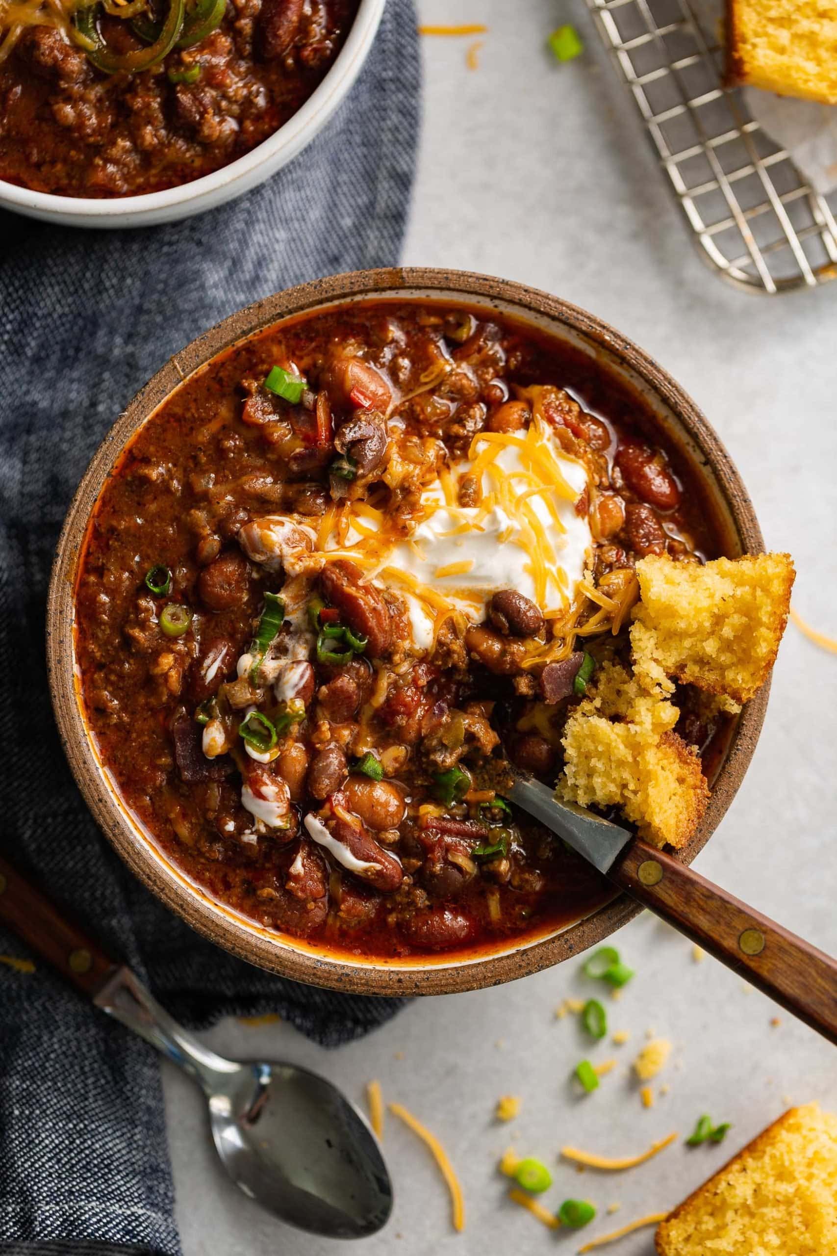 Best Chili Recipe A bowl of the best chili. A spoon is in the bowl. There are beans and ground beef in a rich sauce and the chili is topped with sour cream and shredded cheese.