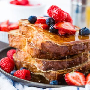 A photo of how to make french toast with a stack of french toast covered in dripping syrup and fresh berries.