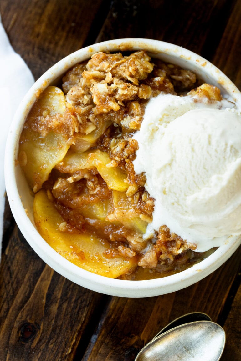 a photo taken over the top of a bowl filled with a serving of apple crisp topped with a melting scoop of vanilla ice cream.