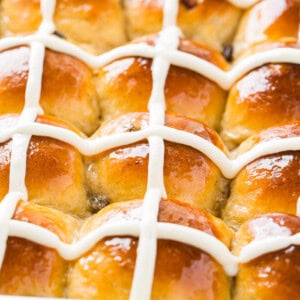 A close up photo of a pan of hot cross buns with white frosting crosses.
