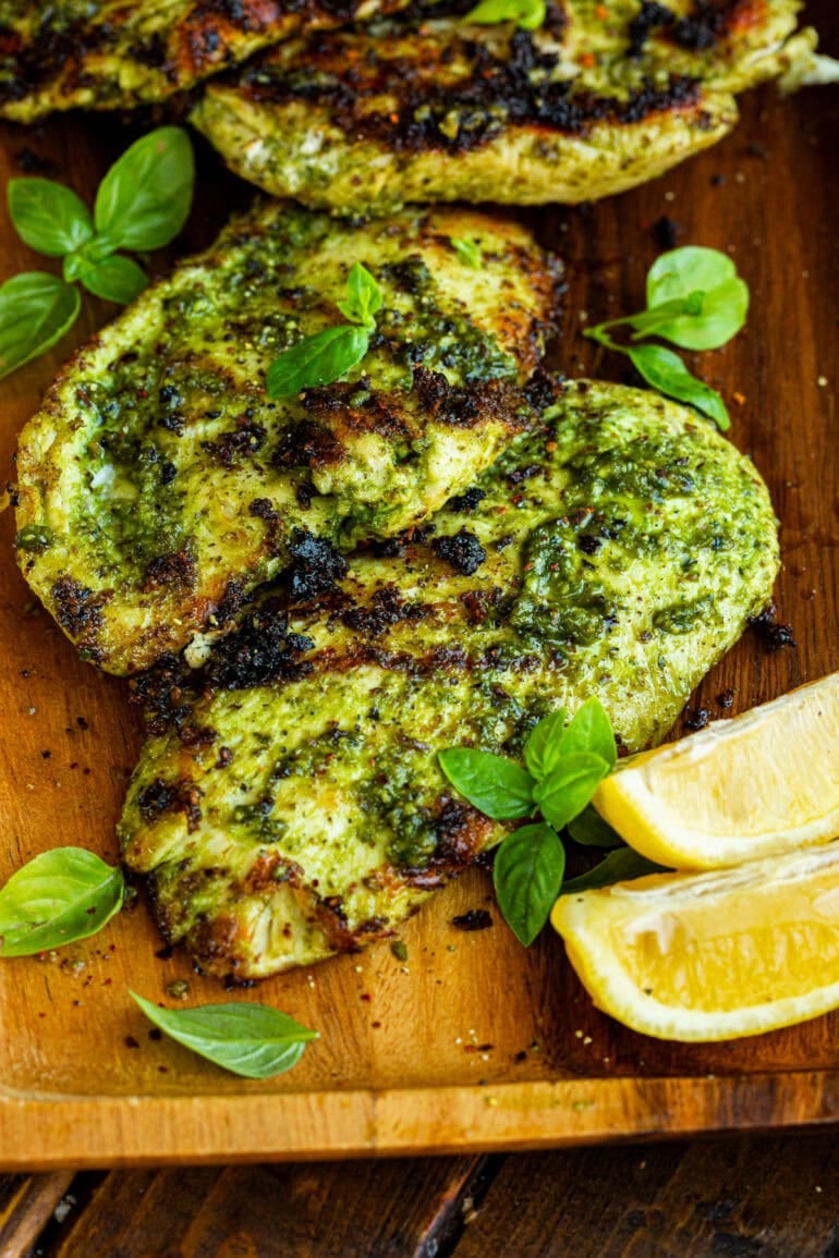 a photo taken over the top of two grilled chicken breasts coated in basil sitting on a cutting board with lemon wedges sitting next to them