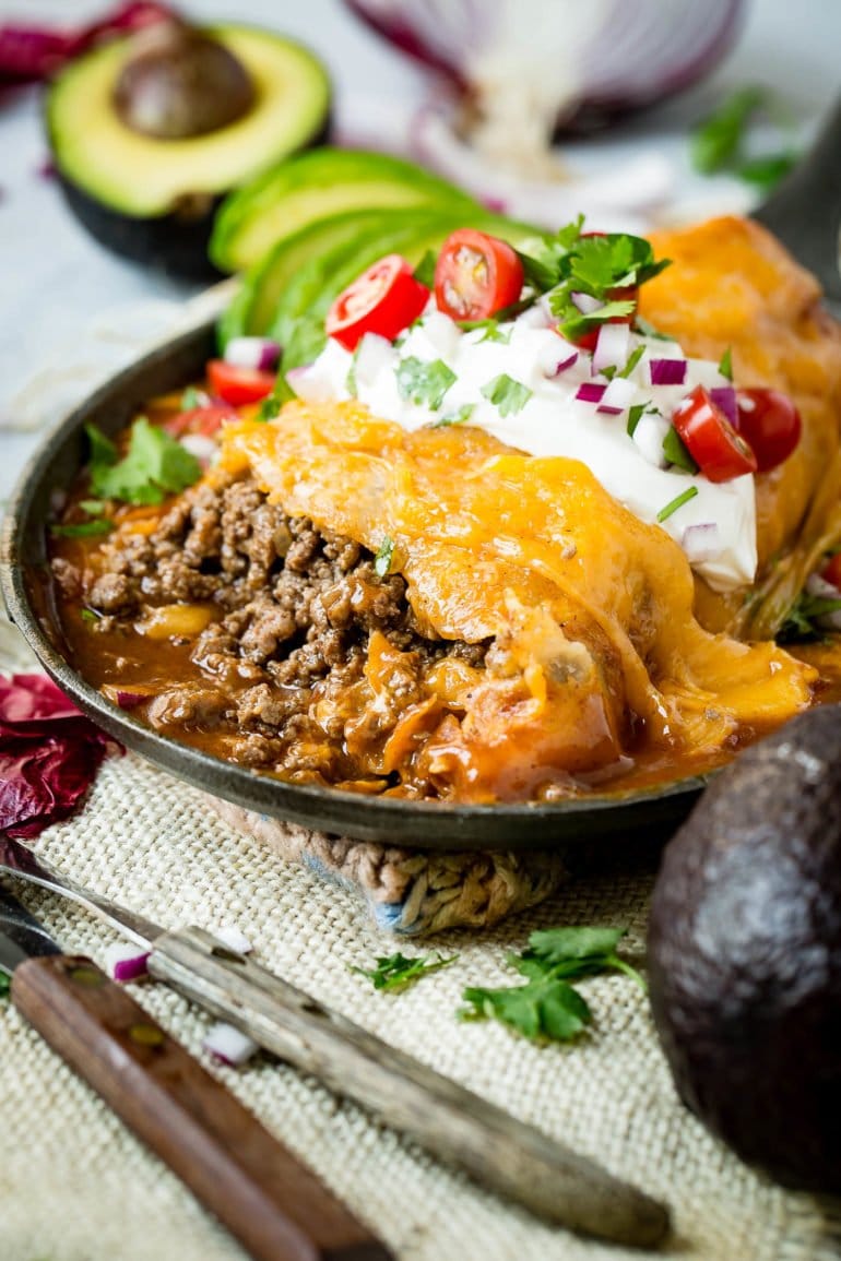 A tortilla wrapped, drenched in enchilada sauce, and covered in gooey, golden cheese.